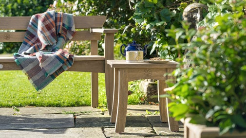 Low shot of a wooden bench and table on a stone patio surrounded by shrubbery